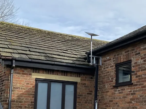 Starlink satellite dish mounted on a roofline bracket of a brick house