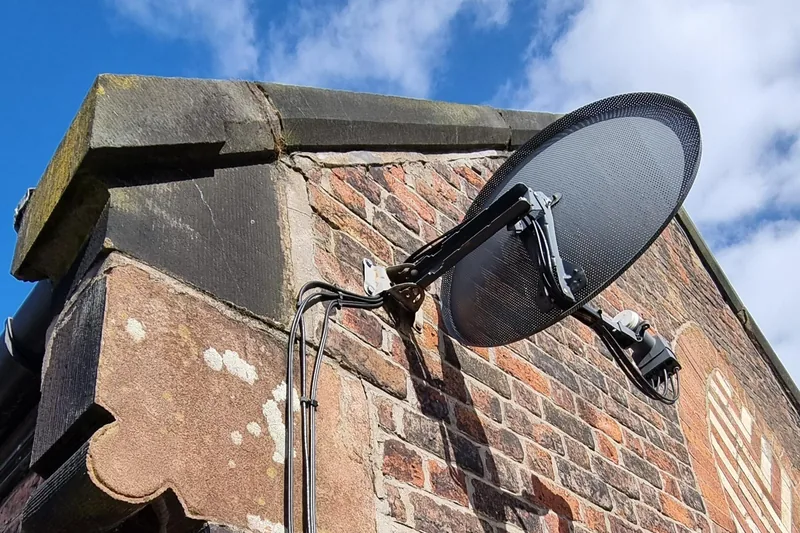 Satellite dish securely mounted on a brick wall with metal bracket