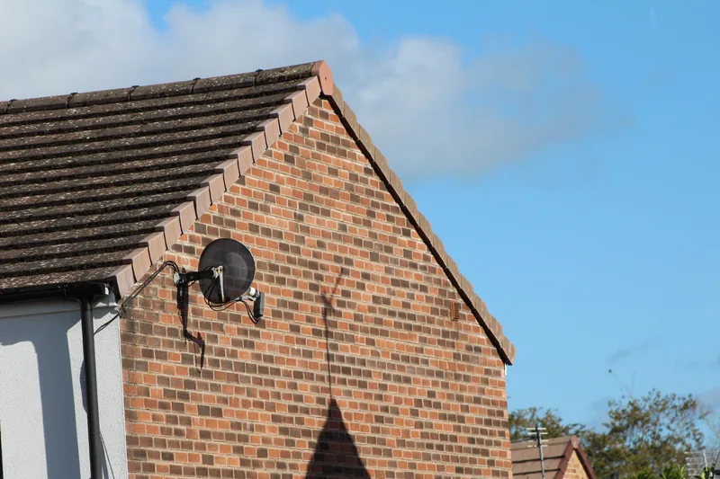 Existing Sky satellite dish with older-style LNB mounted on the brick gable wall of a house